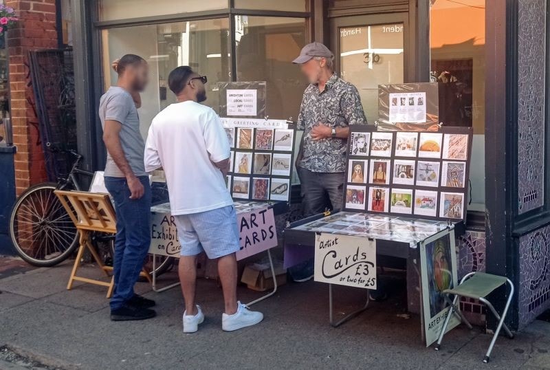 Arist selling cards and prints in front of an empty shop